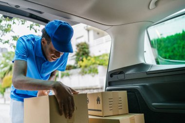 Teslimat işçisi bir arabanın bagajında çeşitli paketler düzenliyor, teslimatlara hazırlanıyor. Lojistik ve paket dağılımı kavramı.