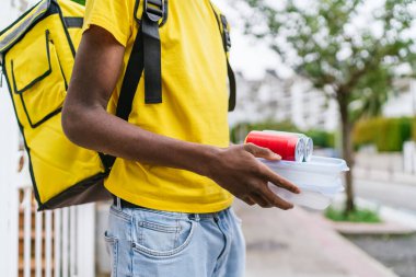 Sarı sırt çantalı bir teslimatçı yiyecek konteynırlarını ve konserveleri tutuyor. Verimli gıda dağıtım hizmeti kavramı.