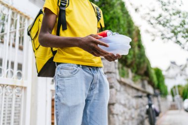 Yemek konteynırları ve teneke kutuları taşıyan teslimatçının yakın çekim fotoğrafı. Verimli gıda teslimatı kavramı.