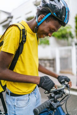 Genç bir Afrikalı, bisikletini bir banliyö caddesinde yiyecek teslimatı için hazırlıyor. Kentsel gıda teslimatı kavramı.