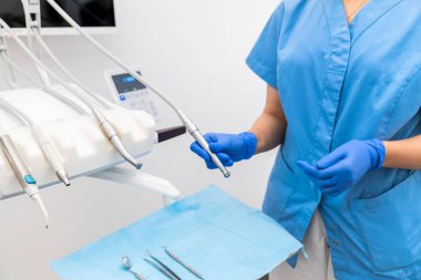 Bir diş hekimi, modern bir klinikte yapılacak bir sonraki randevu için diş hekimliği aletlerini inceler ve hazırlar. Hasta hazırlığı ve profesyonel bakım kavramı.