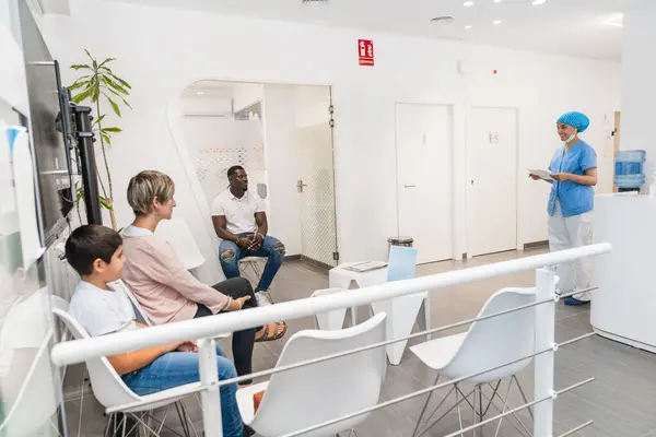 Bir diş hijyenisti randevuları için modern bir kliniğin bekleme salonundaki hastaları arar. Hasta bakımı ve profesyonel sağlık hizmeti kavramı.