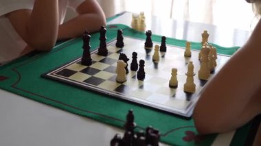 İki çocuk satranç oynuyor. Çocuklardan biri beyaz bir gömlek giyiyor. Diğer çocuk beyaz gömlek ve şort giyiyor.