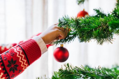 Bir çocuğun elinin ağaca kırmızı bir süs takıp, bayrama hazırlanırken yakın plan çekimi. Festival beklentisi ve tatil gelenekleri kavramı.