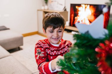Ağacı süslerken neşeli bir çocuk gülümser ve bayram neşesini odanın her tarafına yayar. Tatil neşesi ve çocukluk heyecanı kavramı.