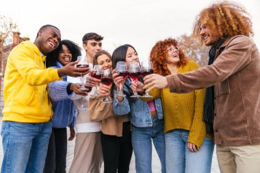 Çok ırklı bir arkadaş grubu kırmızı şarapla kadeh kaldırıyor ve birlikte dışarıda vakit geçiriyorlar.