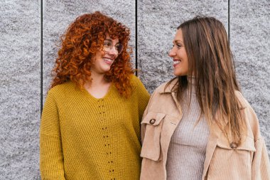 İki arkadaş kışın bir şehir caddesinde gülüp sohbet ediyorlar. Kış kıyafetleriyle arkadaşlıklarını gösteriyorlar.