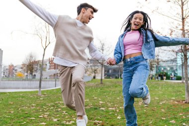 Genç çift el ele tutuşup parka gülerken havaya zıplıyorlar.