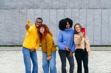 Bir grup çok ırklı arkadaş akıllı telefonlarıyla selfie çekiyor ve birlikte eğleniyorlar.