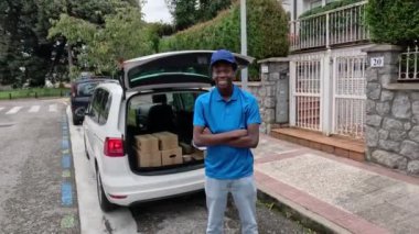 Kollarını kavuşturmuş gülümseyen bir teslimat işçisi teslimatlara hazır paketlerle dolu bir aracın yanında duruyor. Güven ve profesyonel hizmet kavramı.