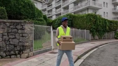 Genç Afrikalı kurye elinde iki paketle mahalleye giriyor. Kentsel alanlarda verimli paket dağıtımı kavramı.