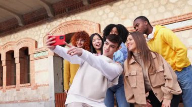 Bir grup genç çok ırklı arkadaş akıllı telefonlarıyla selfie çekiyor, dışarıda birlikte eğleniyorlar.