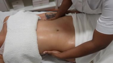 Güzellik uzmanı bir güzellik kliniğinde estetik bir tedaviden dolayı bir kadının karnına lenfatik drenaj masajı yapıyor.