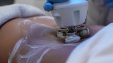 Güzellik uzmanının kadın karnında vücut şekillendirme makinesi kullanmasına yakın çekim.