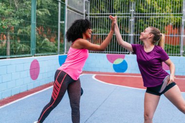 İki çok ırklı bayan arkadaş, renkli bir açık hava sahasında oynanan dostça bir yankesicilik maçında beşlik çakıyor.