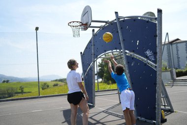 Anne, güneşli bir günde oğlunun basket atışını seyrediyor. Birlikte dışarıda güzel vakit geçiriyorlar.