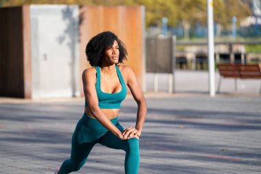 Afro-Amerikan sporcu bir şehir ortamında bacak esnetme, vücut geliştirme ve sağlıklı yaşam tarzı sergiliyor.
