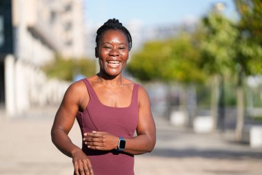 Kendine güveni tam bir zenci kadın şehir parkında mutlu bir şekilde koşuyor, akıllı bir şekilde koşuyor, güneşli bir günde güç ve motivasyon yayıyor.