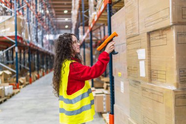 Genç bayan depo çalışanı barkod tarayıcı ile paketleri tarıyor, dağıtım merkezinde envanter ve lojistik yönetiyor.
