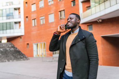 Gülümseyen Afrikalı genç işadamı, modern bir ofis binasının dışında telefon görüşmesi yapıyor, başarılı bir iş gününün tadını çıkarıyor.
