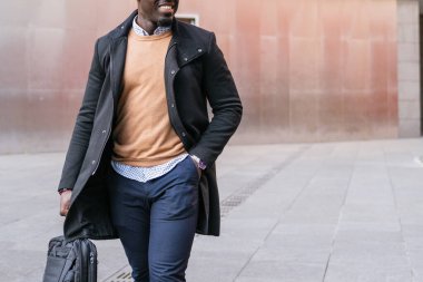 Tanınmayan genç Afrikalı iş adamı gülümseyerek şehirde yürüyor, elinde bir laptop çantası, işe gidiyor.