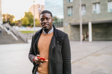 Kendinden emin genç Afrikalı girişimci canlı bir şehir ortamında akıllı bir telefonla iletişim kuruyor, modern iş başarısını ve hırsını somutlaştırıyor.