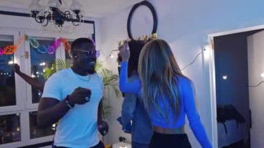 Çoklu etnik arkadaşlar bir ev partisini kutluyorlar, ağır çekimde neşeyle dans ediyorlar, birlikte canlı anılar yaratıyorlar.