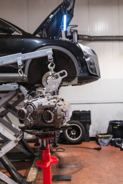 Bir garajda kırmızı desteğe konan şanzıman, bakım veya yenileme işlemleri sırasında hidrolik asansörde kaldırılan bir araba.