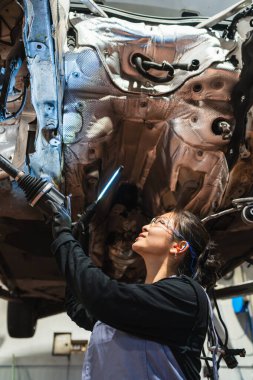 UV ışığı kullanan Asyalı kadın tamirci ve koruyucu gözlük takıyor bir tamircide arabanın bagajını incelerken.
