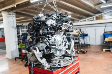 Modern araba motoru, yoğun bir tamirhanenin zincirinden askıya alınarak otomotiv bakımı ve teknolojisinin karmaşık detaylarını gözler önüne seriyor.