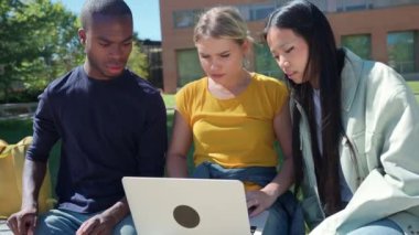 Açık havada dizüstü bilgisayarda işbirliği yapan çok ırklı üniversite öğrencileri, güneşli bir parkta tartışmalara ve fikirlerini paylaşıyorlar.