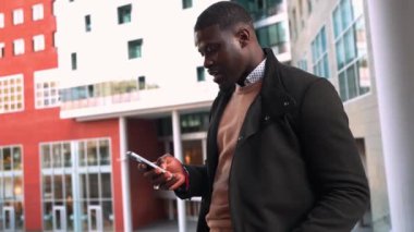 Modern bir şehir ortamında akıllı telefonunu kullanan genç bir Afrikalı iş adamının yavaş çekim videosu.