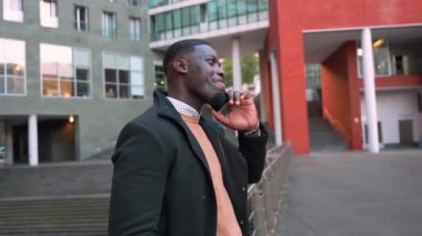 Afrikalı işadamı cep telefonuyla modern ofis binasının önünde güven içinde konuşuyor, mesleki başarı ve olumlu iletişimi ifade ediyor