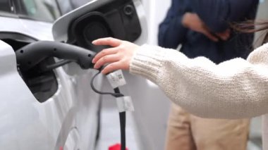 Kadın yavaş çekimde elektrikli araba şarjını beyaz araca takıyor, sürdürülebilir ulaşım teknolojisi ve temiz enerji taahhüdü gösteriyor