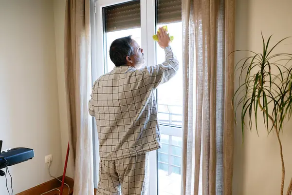 Emekli bir adam dairesinde cam siliyor, ev hayatından zevk alıyor ve temizliğini koruyor.