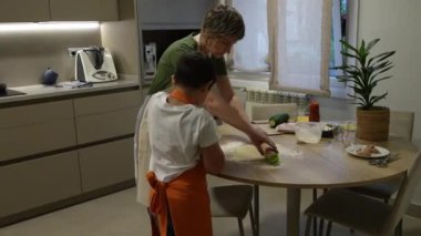Becerikli bir anne, mutfak masasında pizza hamurunu dikkatlice sararken ve yemek pişirme anlarında yemek pişirme bilgisini paylaşırken küçük oğluna rehberlik ediyor.