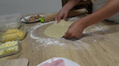 Profesyonel şef un ahşap yüzeyde pizza hamuru yoğuruyor, geleneksel İtalyan mutfağını çalışma alanını çevreleyen taze malzemelerle hazırlıyor.