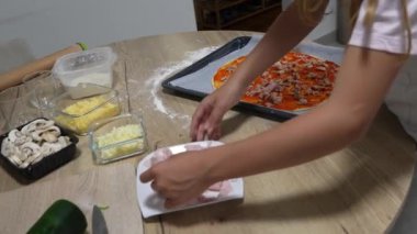 Çocuklar pizzacıya ton balığı ve jambon ekliyor, mutfaklarında ev yapımı pizza hazırlıyorlar.