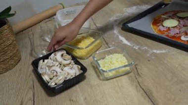 Genç aşçılar mutfaktaki bir pizzacıya mantar, kabak, jambon ve peynir ekliyor.