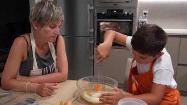 Anne, oğlunun cam bir kasede yumurta çırpışını izliyor ve evlerinin mutfağında birlikte sünger keki hazırlıyor.