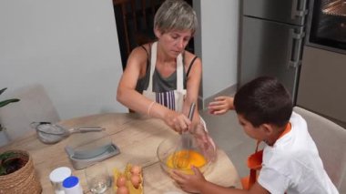 Anne, oğluna yumurta çırpma konusunda rehberlik ediyor. Mutfakta birlikte kek pişirmek için temel bir adım.