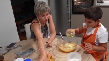 Anne oğluna sünger keki yapmayı öğretiyor, malzemeler ekliyor ve cam kasede birlikte çırpıyor.
