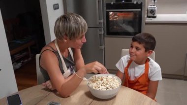Önlük takan anne ve oğul modern mutfaklarında taze patlamış mısır tadıyorlar.