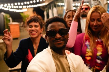 Genç çoklu etnik arkadaşlar dans ediyor ve neşeli bir partide eğleniyorlar, müzikten zevk alıyorlar ve birlikte neşeli anılar yaratıyorlar.