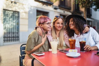 Açık bir kafede içkileri kucaklayan ve eğlenen üç neşeli genç kadın, beraberlik ve dostluk anlarını paylaşıyorlar.