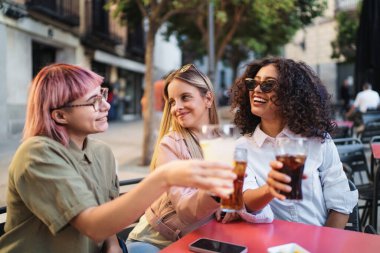 Üç neşeli genç bayan açık hava kafeteryasında içkilerimizi yudumlayarak kutlama yapıyorlar.