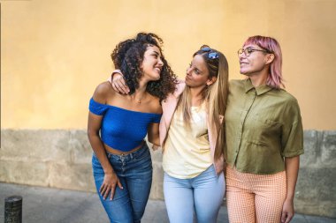 Üç neşeli bayan arkadaş, güneşli bir günde birbirlerine sarılıp gülümsüyorlar.