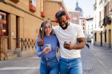 Müzikten hoşlanan ve sokakta yürürken akıllı telefon kullanan genç bir çift.