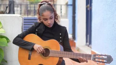Genç bayan müzisyen akustik gitar çalışıyor, açık havada tutkulu bir şekilde oturuyor ve gün ışığında müzik performansını vurguluyor.