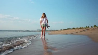 Kız deniz kıyısında yalınayak yürüyor, gün batımında kumsalın sessizliğinin tadını çıkarıyor.